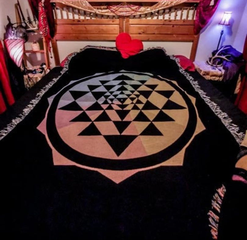 Room with a king sized bed with a cotton blanket and a rainbow Sri Yantra design with fringe.